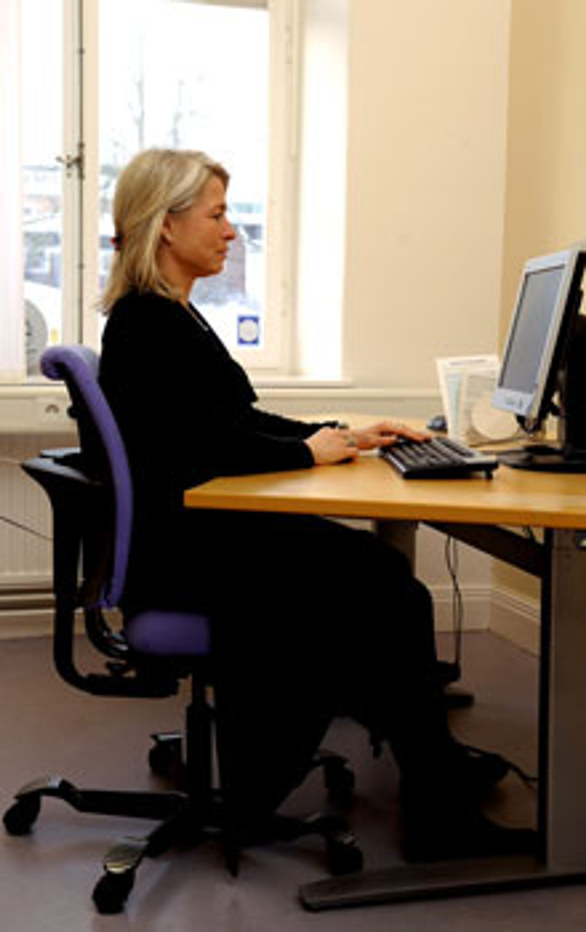 Ergonom Annika Gladh demonstrerer riktig stilling ved datamaskinen. Beina er godt plantet på gulvet, og bord og stol er innstilt slik at armene hviler på bordet. Ryggen holdes rett, men man skal beholde naturlige kurver i nakke og korsrygg. Blikket går rett fram. FOTO: Anders Wiklund/Scanpix