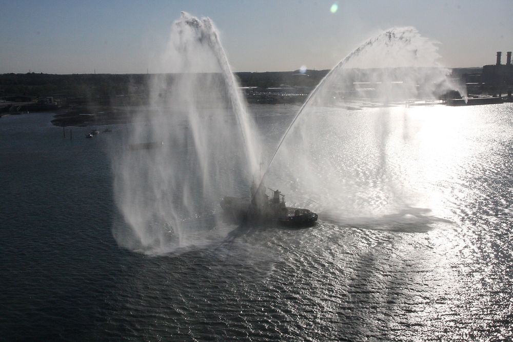 En liten taubåt feirer Anthem of the Seas med brannvernkanonene. 