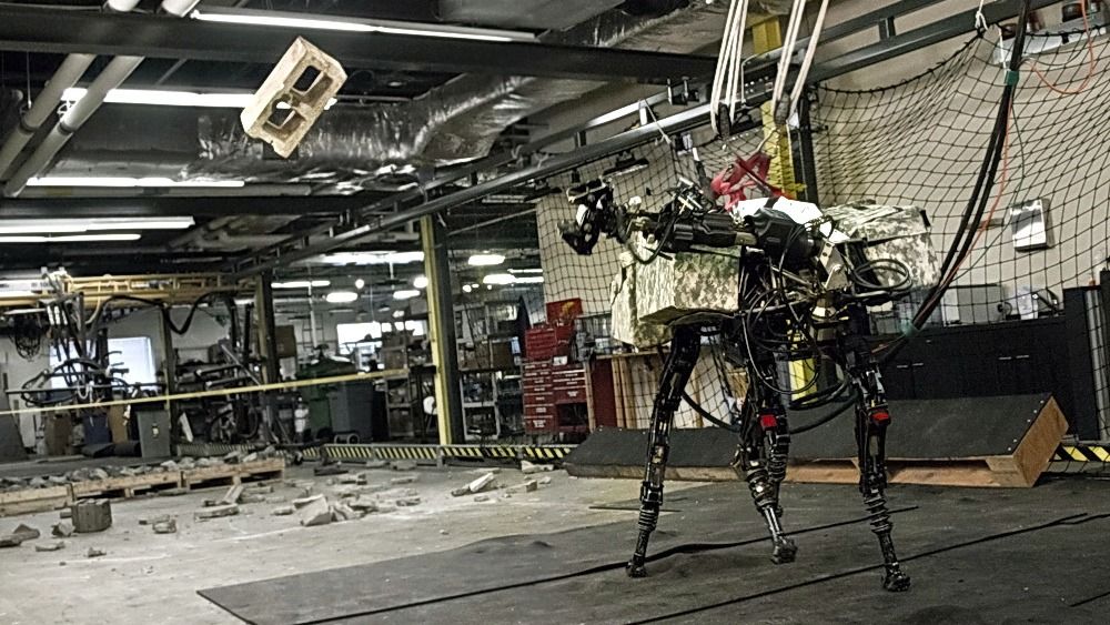 BigDog bruker både den nye armen, beina og kroppen for å kaste den tunge betongblokken veggimellom. Foto: Boston Dynamics