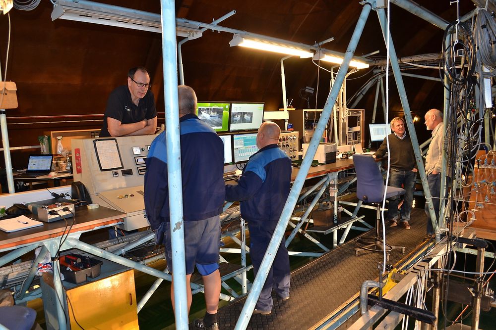 SNART KLARE: Teknisk direktør Tor Kolbjørn Livgård i SES Europe i samtale med Hans Anderson og Gheorghe Popa fra SSPA. I bakgrunnen SSPAs prosjektleder Matz Brown og skipsingeniør og hydrordynamiker Hans Liljenberg. Alle befinnersom om bord på slepevogna. Modellen flyter på vannet nede til høyre.