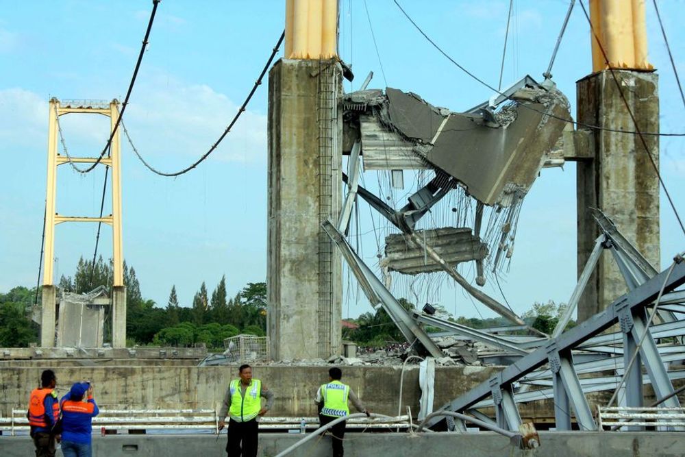 Indonesiske politimenn foran den ødelagte broen som kollapset lørdag. Fire personer er bekreftet døde, og det letes fortsatt etter savnede søndag.