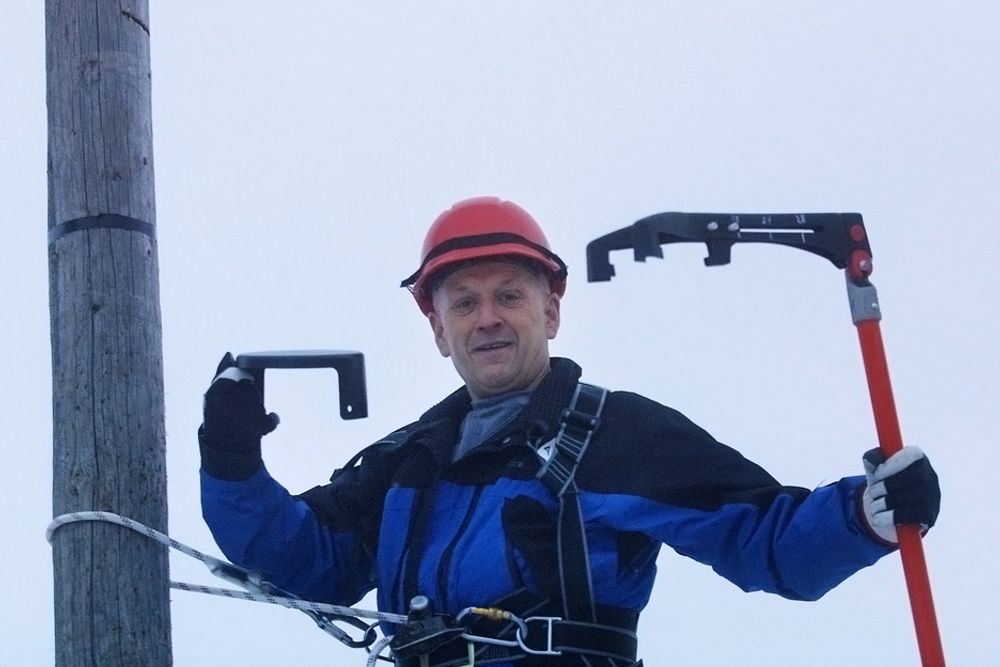 Oppfinner Roald Engan holder topphetta mens montør Stian Brodersen skrur den fast til stolpen ved hjelp av en drill montert på en lang stang.