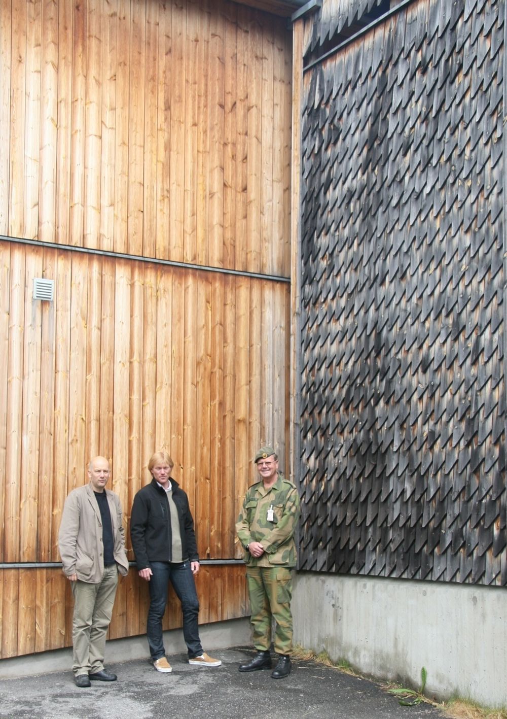 VARIERT: Her viser, fra venstre, arkitekt Arvid Rønsen Ruud, Prosjektsjef Jens Levi Moldestad og ansvarlig for drift og vedlikehold Åge Mohaugen hvordan fargeutviklingen på ubehandlet trevirke ikke er ensartet.  Bilde fra Rena Leir