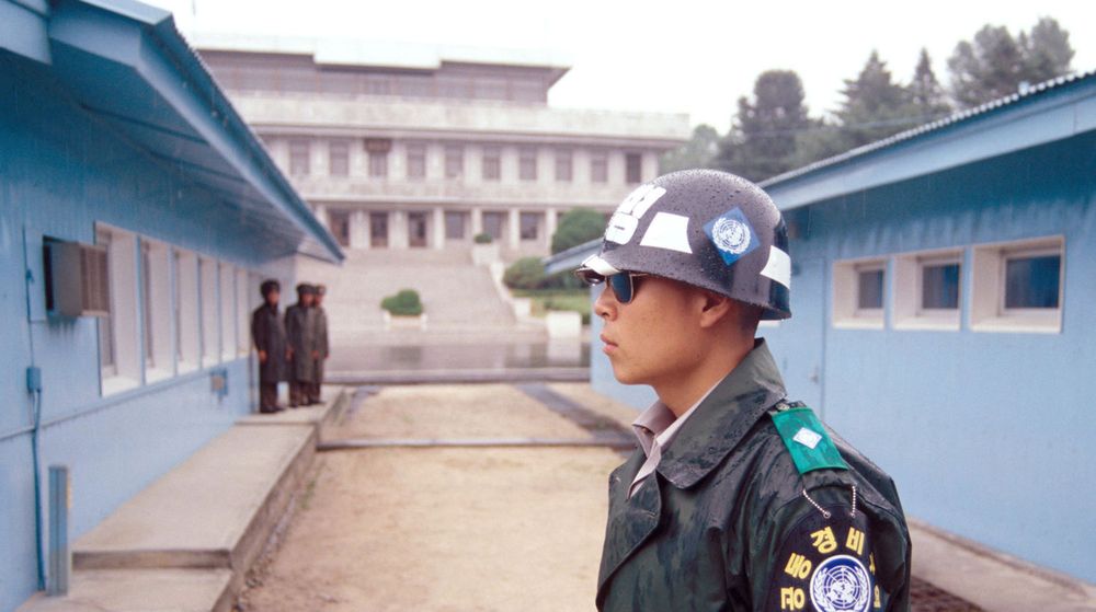 En sørkoreansk grensevakt med steinansikt og mørke solbriller står i full beredskap i DMZ-zonen. De blå husene på bildet markerer det faktiske skillet mellom Nord-Korea og Sør-Korea.