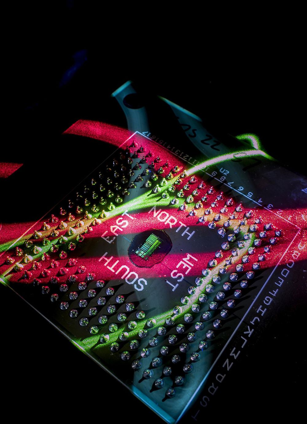 Den elektronikk-fotonikk-baserte prosessorbrikken kommuniserer med omverdenen ved hjelp av lys. De røde og grønne lysbåndene på bildet er lagt til kun for effektens skyld.