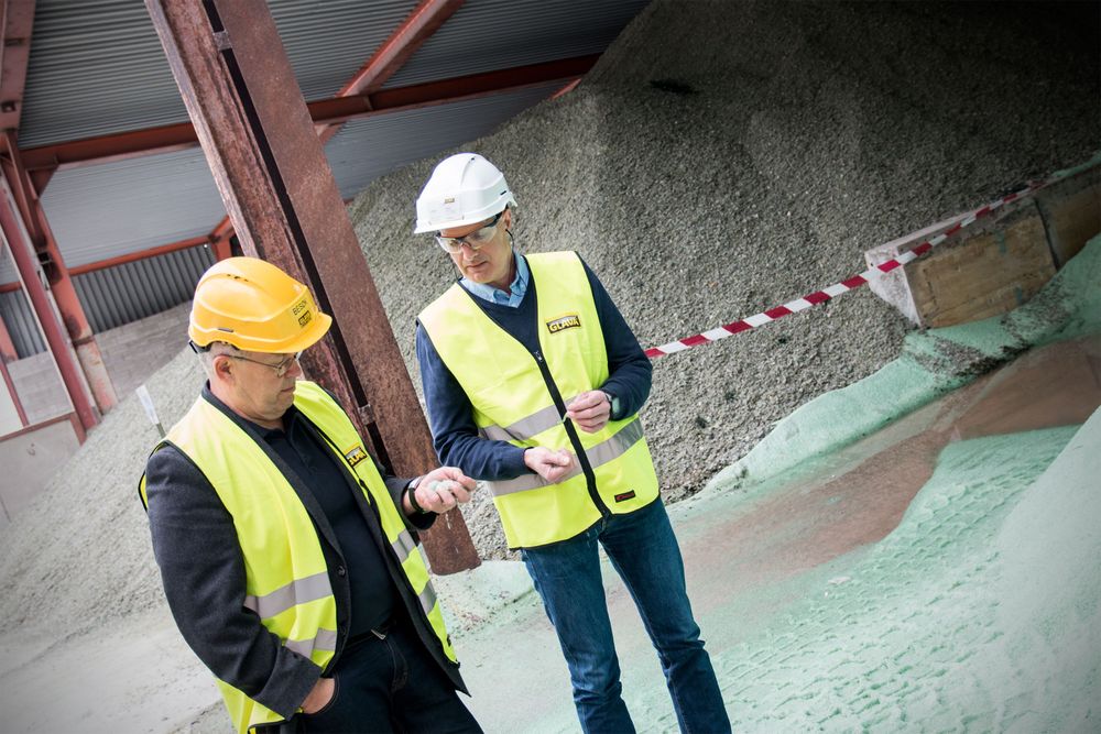 Administrerende direktør Jon Karlsen (t.v) og fabrikksjef Jan Dag Aaen står foran råmaterialet til glassullen: resirkulert glass i store mengder.
