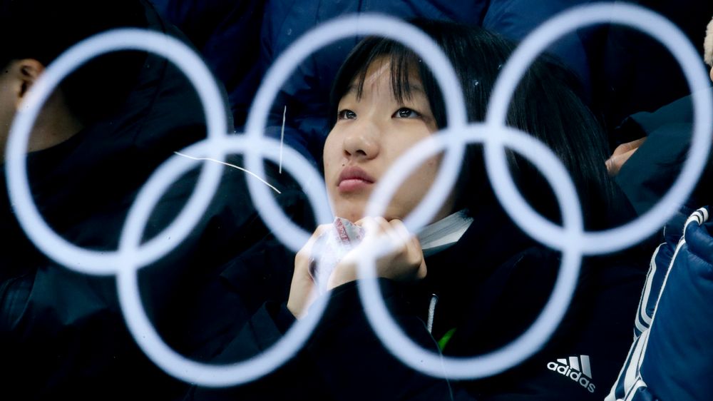 Illustrasjonsbilde: De olympiske ringene reflektert i et glass. En kvinnelig tilskuer sitter bak glasset og ser på mixed double-semifinalen i curling mellom Canada og Norge under de olympiske vinterlekene i Pyeongchang, Sør-Korea.