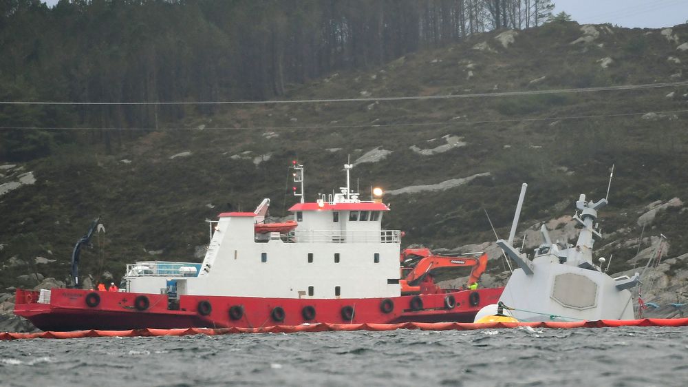 En båt med bergingsmannskaper ved den havarerte fregatten. Helge Ingstad ligger nå nesten helt under vann, etter at flere vaiere som har holdt skipet fast, har løsnet.