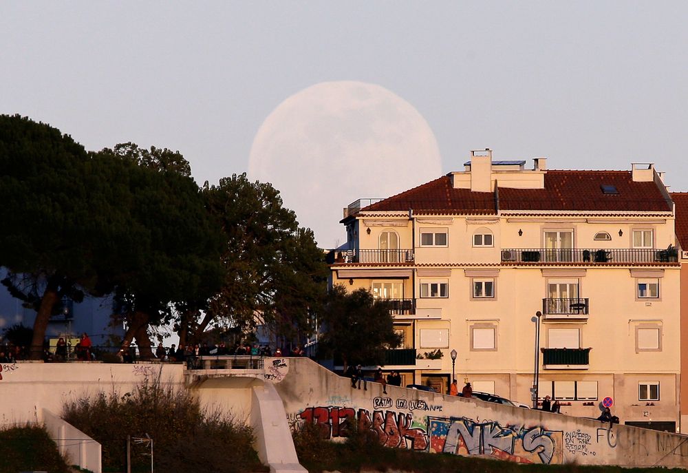 Fullmånen på vei opp over Lisboa i Portugal søndag kveld.