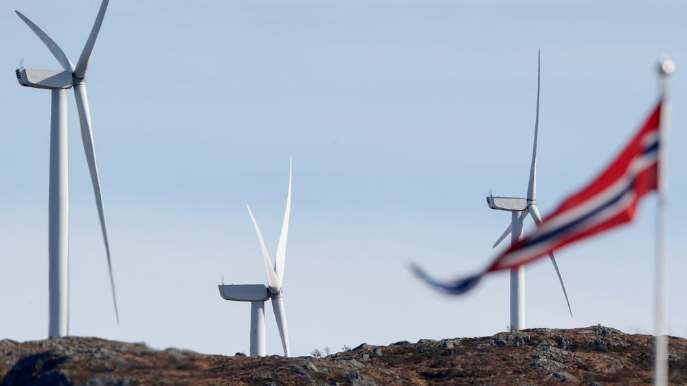 Vimpel i Fitjar sentrum med tre av vindturbinene i Midtfjellet vindpark i Fitjar kommune i bakgrunnen.