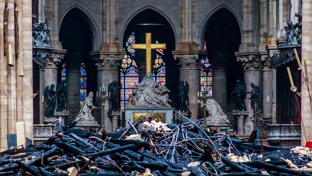 Utbrente rester av taket ligger inne i Notre-Dame dagen etter brannen mandag. Det som ser ut som intakte vokslys, står på staker i kantene av bildet.