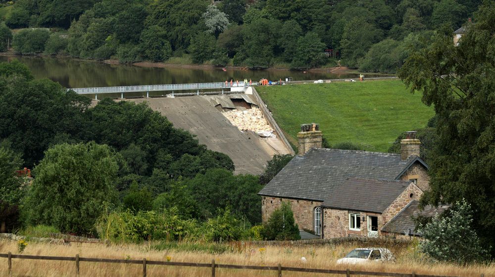 Vannmagasinet Toddbrook Reservoir like ved den lille byen Whaley Bridge i Derbyshire i England lørdag. Siden da har hjelpemannskaper pumpet vannstanden ned ytterligere 3,5 meter og helikoptre har sluppet 530 tonn sandsekker for forsterke den ødelagte murveggen.