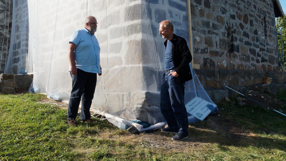Kirkeverge Ole Jakob Dyrnes, til venstre, sammen med Morten Stige ved hjørnet der det er setningsskader. Sprekker oppstår i muren, som må sikres bedre.