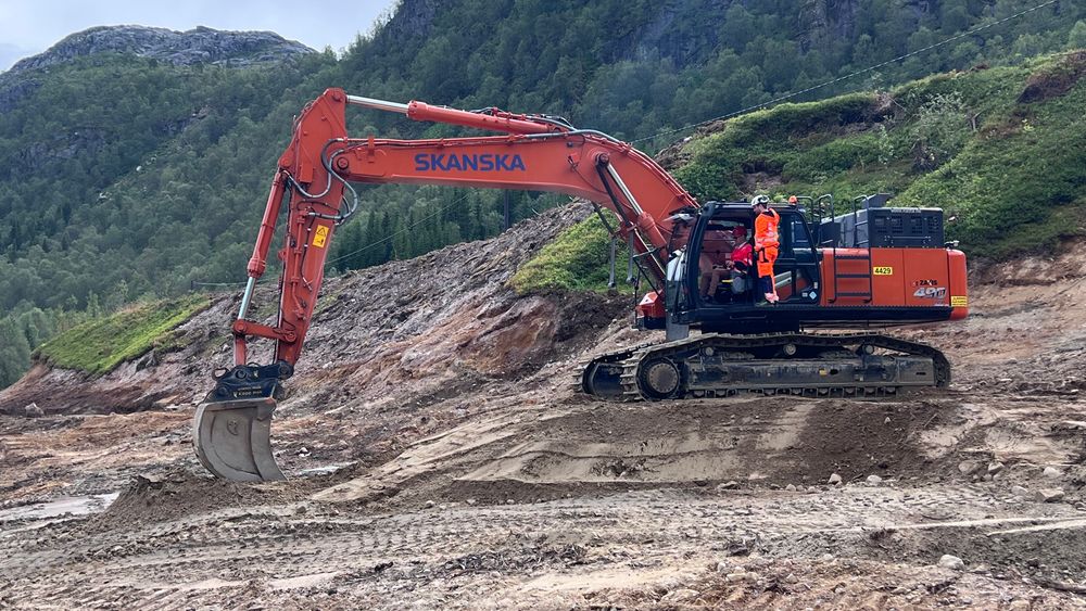 Samferdselsminister Jon-Ivar Nygard tar første spadetak på Hålogalandsveien fra gravemaskin. Godt hjulpet av en ansatt i Skanska.