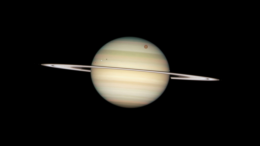 24. februar 2009 passerte fire av Saturns måner foran Hubble teleskopet. Fra venstre til høyre er rekkefølgen på månene: Enceladus, Dione, og den store oransje er Titan, deretter Mimas. På grunn av solens posisjon er hver av månene fulgt av sin egen skygge. 