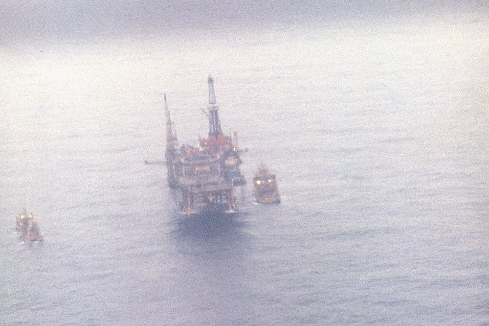 Bilde av boligplattformen Alexander Kielland dagen etter at den mistet ett av beina og kantret i Nordsjøen den 27. mars 1980. På bildet ser man de fire gjenværende beina på den veltede plattformen som stikker opp av vannet.