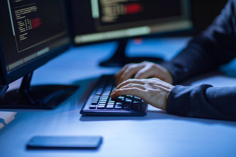 cybercrime, hacking and technology concept - hands of hacker in dark room writing code or using computer virus program for cyber attack