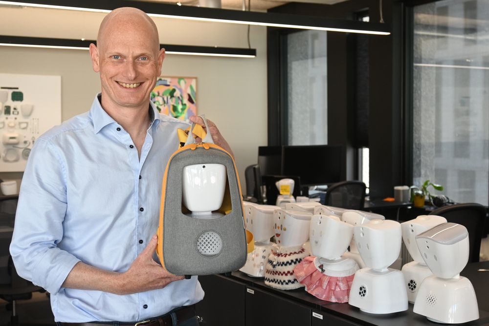 Morten Jørgensen, sjef i No Isolation, sammen med et knippe pyntede AV1-roboter. Her med en spesialutviklet ryggsekk for AV1. 
