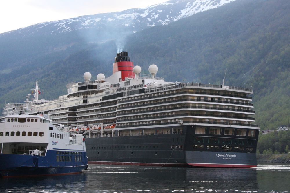 Cruiseskipet Queen Victoria på vei til kai i Flåm for noen år siden. Skipet kan fortsette med det til 2032, mens ferga til venstre må skiftes ut med nullutslipp.