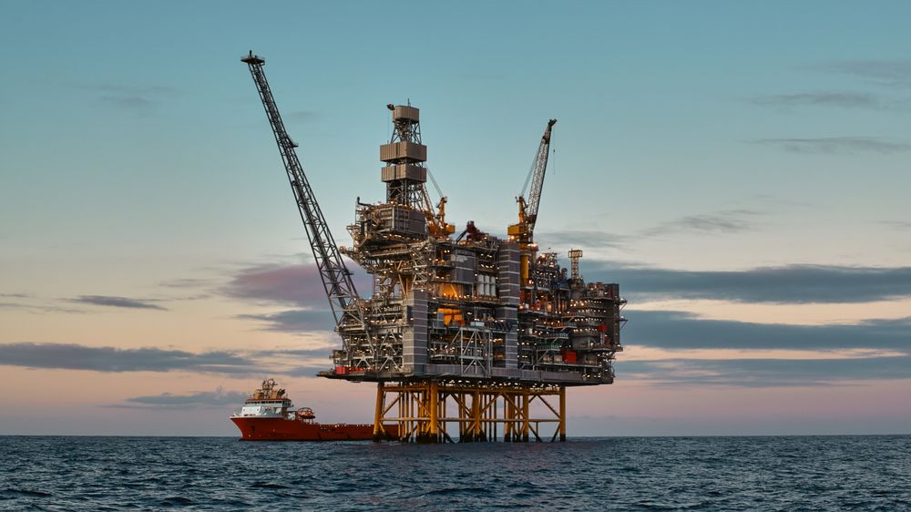 Offshore oil and gas jackup platform, during cargo operations with supply vessel in the sea and beautiful colourful sunset sky.