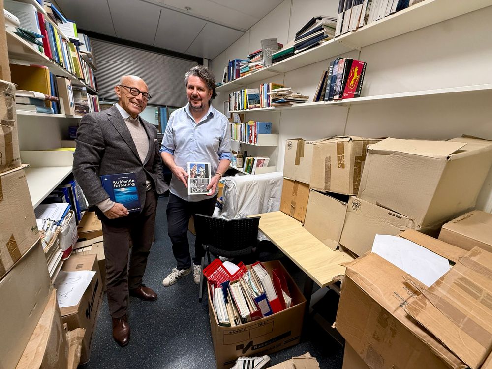 Viktor Wikstrøm (t.v.) og Pål Nygaard kan mye om historien til Institutt for energiteknikk. Her er de avbildet med hver sin historiebok på sistnevntes «professorkontor». 
