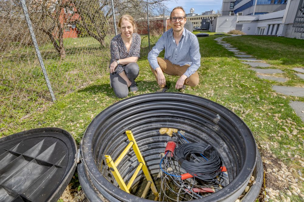 Seniorforsker Guro K. Svendsen og forskningsleder Volker Oye i bakhagen til Norsar på Kjeller, hvor er strukket fiberkabler mellom slike brønner som den på bildet. Kablene brukes til å registrere rystelser i bakken. 