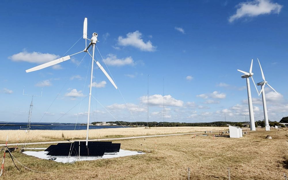 KiteX har fått mulighet til å teste sin nye lettvektsvindturbin på det gamle forsøksområdet på Risø. Til høyre ser vi to eldre, tradisjonelle vindmøller, og i horisonten kan den nedlagte tungtvannsreaktoren DR2 skimtes.