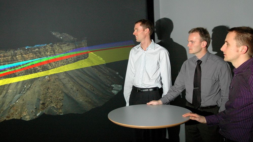 SER FORTIDEN: I det nye  visualiseringslaboratoriet kan studenter og forskere se hvordan avsetningen i jordoverflaten har endret seg over tid. For å bedre oljeutvinningen ser Simon Buckley. Jan Tveranger og Håvard Drange Enge etter tynne flater med hardere materialet som kan hindre gjennomstømming av olje og gass. De forskjellige fargede feltene er slike flater i en fjellformasjon i Utah, USA.