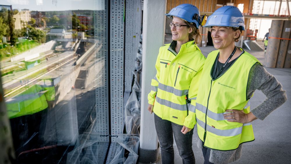 Magnhild Kallhovd og Bodil Motzke i Undervisningsbygg ser ut av vinduet fra flerbrukshallen på Brynseng skole som her var under oppføring. Nå håper de å ha løst problemet med overskuddstrømmen ved skolen.