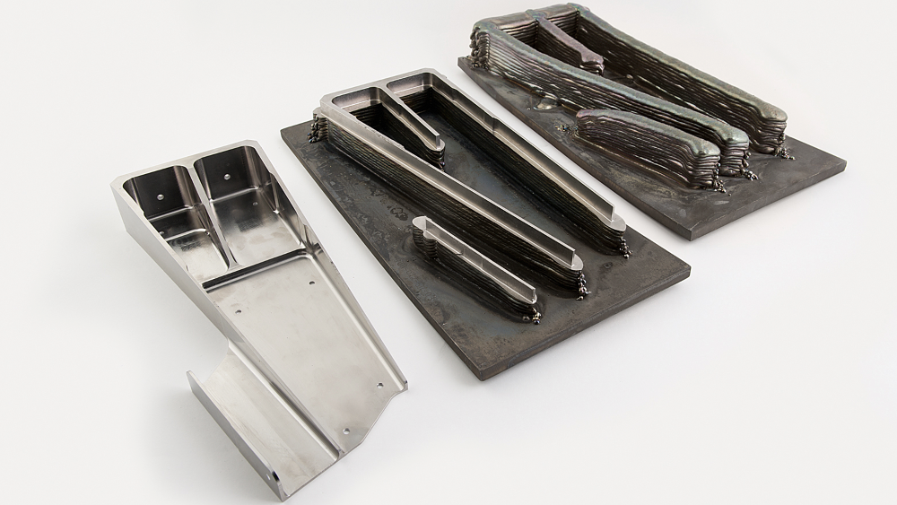Bildet illustrerer veien fra 3D-printet del til ferdig del. Hadde delen blitt frest ut, måtte man startet med en metallblokk med målene til delens ytterkanter. Kvalitetskrav gjør at titanet som freses bort ikke kan gjenbrukes. Det er derfor svært viktig med så lite svinn som mulig.