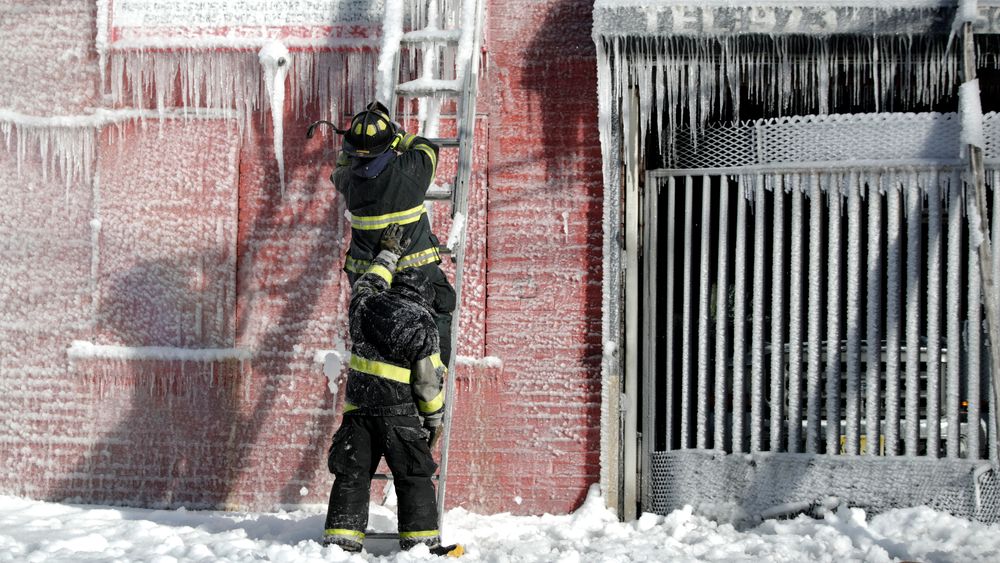 En brannmann støttes opp av en kollega mens kan kapper is av en stige etter å ha bidratt til å slukke en boligbrann i Newark, USA.