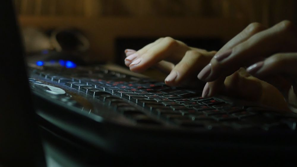 fingers of female on laptop, working late at night, blank blurred white screen as background, dark tone