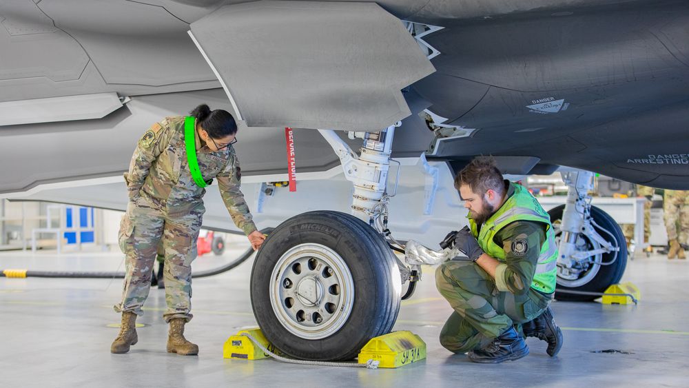 Norsk og amerikansk tekniker jobber på et amerikansk F-35A i et shelter på Ørland flystasjon.