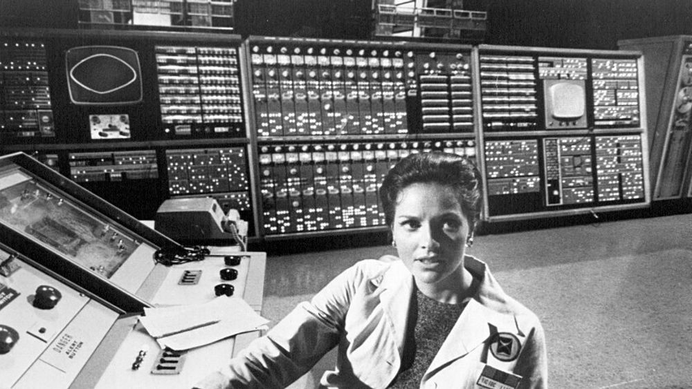 I bakgrunnen sees en datamaskin med paneler fra AN/FSQ-7.  Bildet er fra TV-serien The Time Tunnel fra 1966. Kvinnen er skuespilleren Lee Meriwether som spilte doktor Ann MacGregor i serien.