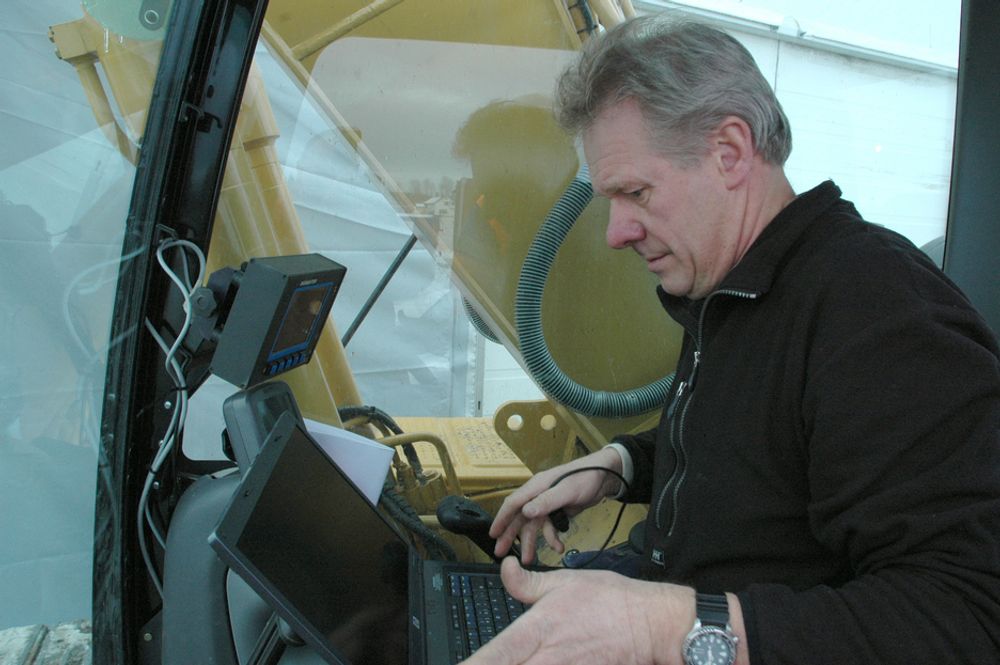OPPDATERING:Jan Floberg legger inn de siste oppdateringene og justerer målene på det kombinerte maskinstyrings- og GPS-anlegget i nok en gravemaskin. Boksen øverst er datamaskinen  med skjerm og kanpper til betjening.