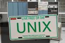 Bilskilt brukt i markedsføringen av UNIX, foran et tilsvarende system som det Unix først ble utviklet for – DEC PDP-7 – fotografert ved Universitetet i Oslo i 2005.