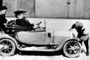 Denne lille Cadillac-elbilen er faktisk kongehusets aller første bil. Kronprins Olav fikk den i julegave fra dronning Alexandra av England. Her sitter han bak rattet sammen med tre kamerater. I baksetet redaktør Strøm, de to andre er engelske gutter, brødrene Brown. Bilen eies i dag av Teknisk Museum.