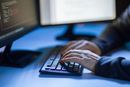 cybercrime, hacking and technology concept - hands of hacker in dark room writing code or using comp ...