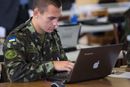 En soldat i med Ukrainas flagg på skulderen sitter foran en laptop.