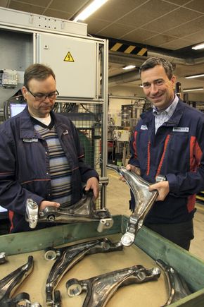 Hans Petter Kristiansen (t.v.) med ferdig montert hjuloppheng til Volvos XC 90-serie. Christopher M. Braathen med delen før den sendes inn i den robotiserte monteringslinjen. <i>Foto: Tore Stensvold</i>