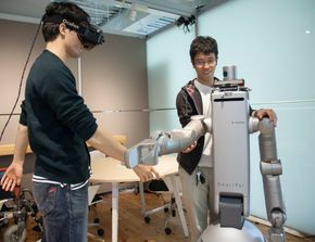 Masterstudenten Akio Shigekane og Yuta Watanabe, sammen med en robot som kan bidra innen pleie. <i>Foto: Nils Olav Mevatne</i>