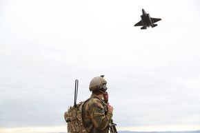 Et F-35A passerer lavt over en soldat på Tarva skytefelt. Luftforsvaret har nå erklært IOC med de nye kampflyene, det vil si at de er operative. <i>Foto:  Torbjørn Kjosvold / Forsvaret</i>