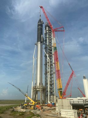 En kran løftet Starship opp på toppen av Super Heavy-raketten sist fredag, og som man kan se, er arbeidet med oppskytningstårnet nesten fullført. <i>Foto:  Elon Musk</i>