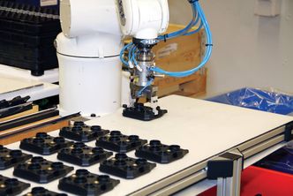 KA Raufoss har fått hjelp av Sintef Manufacturing til å skreddersy automatisert fabrikasjon og montasje. Manifolder flyttet fra matebånd til en mellomstasjon der de blir stilt på skrå. Roboten kan dermed gripe dem uten å blokkere hullene for bremserørskoblingene. Foto: Joachim Seehusen