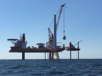 Små hjelpere: Installasjonsskipet Brave Tern assisteres av tre små amerikanske jackup-fartøy, hver med tre ben (til høyre), som leverer vindturbin-deler til installasjonsfartøyet. Her løftes nacellen (generatoren) til den første vindmøllen. Foto: Deepwater Wind