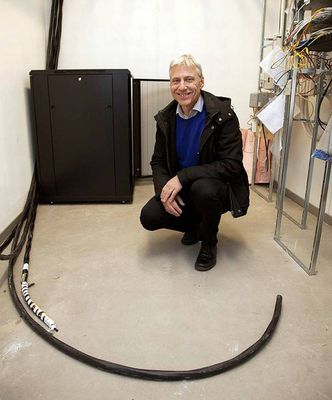 Likestrømsnettets kjerne er en vekselretter (inverter) fra Ferroamp. Det er et svart skap som fungerer som en bro mellom husets vanlige vekselstrømnett og det nye likestrømnettet. Vasakronans Ulf Näslund viser kablene som straks skal kobles inn. Foto: Jörgen Appelgren