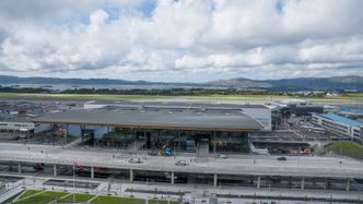 Terminal 3 ved Bergen lufthavn Flesland. En bro foran terminalen frakter reisende til og fra. I bakgrunnen den eksisterende terminal 2. Foto:  Eirik Helland Urke