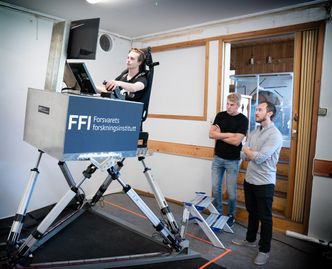 Victor Urnes prøver seg i simulatoren, mens Hans Anders Gjerland og Nikolai Grov Roald følger med. Foto: Eirik Helland Urke