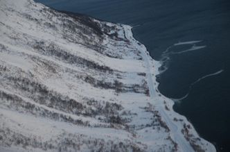 Et snøskred er løst ut med sprengladning fra helikopter ved Singla. Skredet har passert fylkesveien og havnet i sjøen. Foto:  Troms fylkeskommune