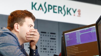 En mannsperson som er ansatt i ved viruslaben til Kaspersky Lab sitter foran en pc. I bakgrunnen sees et skilt med logoen til selskapet.